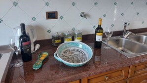 En køkkenbordplade med en vinflaske, et glas, en skål spaghetti og to krydderibøger.