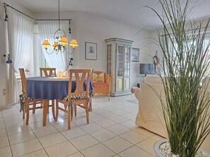Een eetgedeelte met een ronde tafel, stoelen en een kroonluchter. Achtergrond is een bank en een kast.