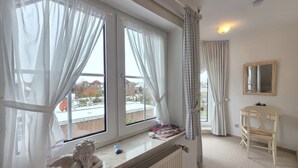 Una habitación con un ventanal grande, un radiador, una mesita con una silla y un espejo en la pared.
