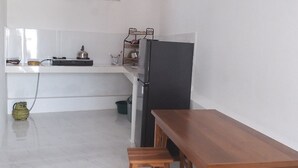 A kitchen with a wooden table and stools, a refrigerator, and a gas stove. - Clean & Affordable Homestay in South Kuta. Simple, Cozy, and Convenient (Badung)