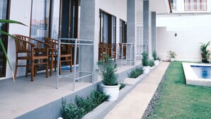 A modern building with a covered outdoor area featuring wooden chairs and tables, a small garden, and a pool. - Clean & Affordable Homestay in South Kuta. Simple, Cozy, and Convenient (Badung)