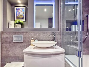 Une salle de bain moderne avec un lavabo blanc, un miroir, un tableau encadré et un espace douche.