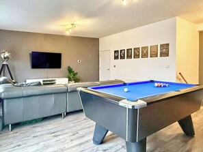 Un salon moderne avec une table de billard, un canapé, un téléviseur et un mur décoré de tableaux encadrés.