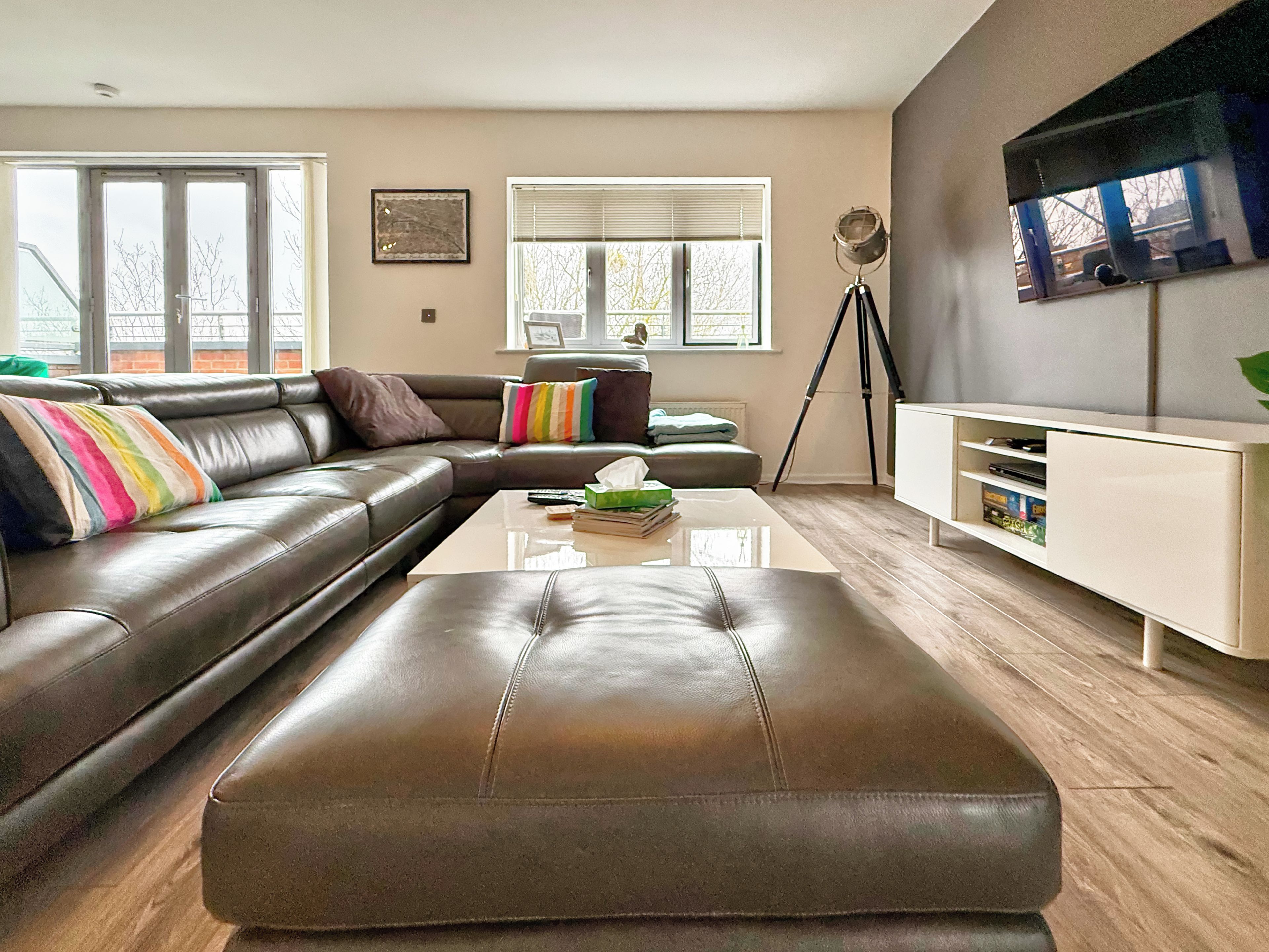 Un salon moderne avec un canapé en cuir, une table basse en verre et un meuble de rangement blanc pour les appareils électroniques.