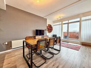 A modern living room with a dining table, chairs, a television, and a bookshelf. - Split level unique large 2BDR apartment (Chelmsford)