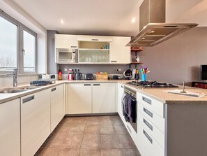 Une cuisine moderne avec des meubles blancs, un four à micro-ondes, une cuisinière à gaz et une fenêtre qui laisse entrer la lumière naturelle.