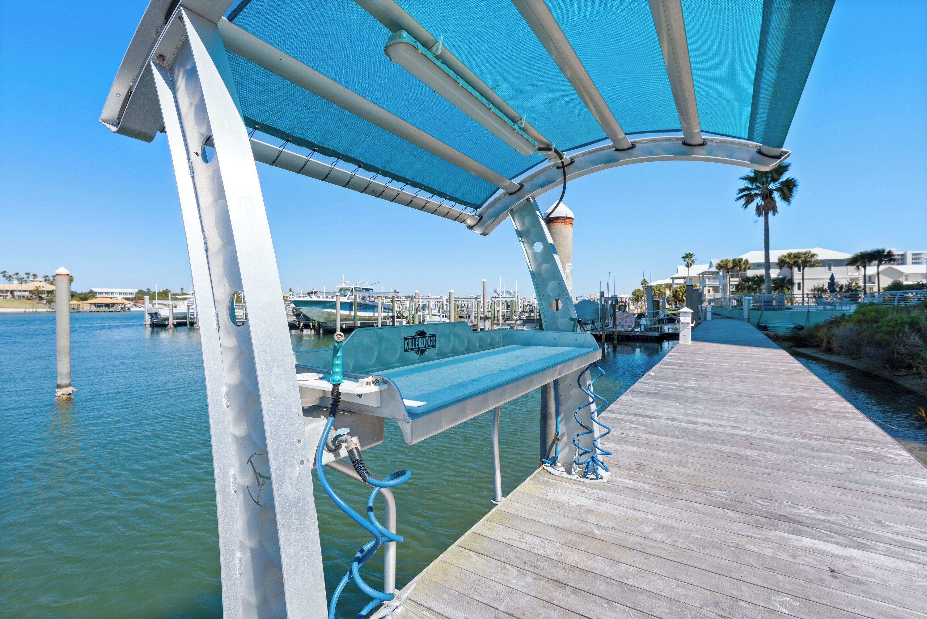 A wooden dock extending into calm water, with a metal structure overhead providing shade.