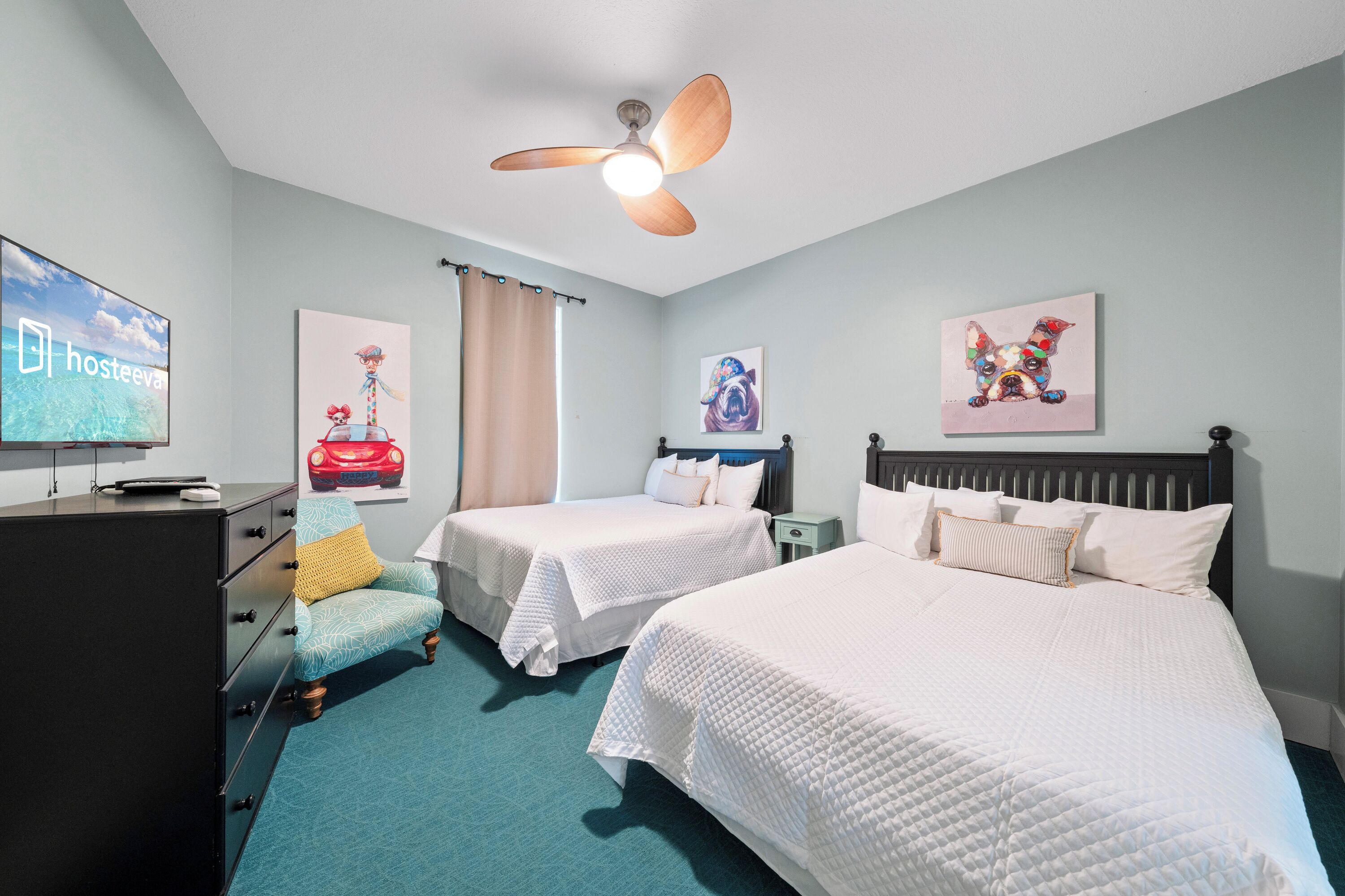 Habitación de hotel con dos camas, ventilador de techo, obras de arte en las paredes, televisor y escritorio con computadora.