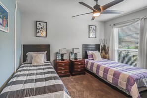 Een slaapkamer met twee bedden, een plafondventilator en een raam met zonwering.