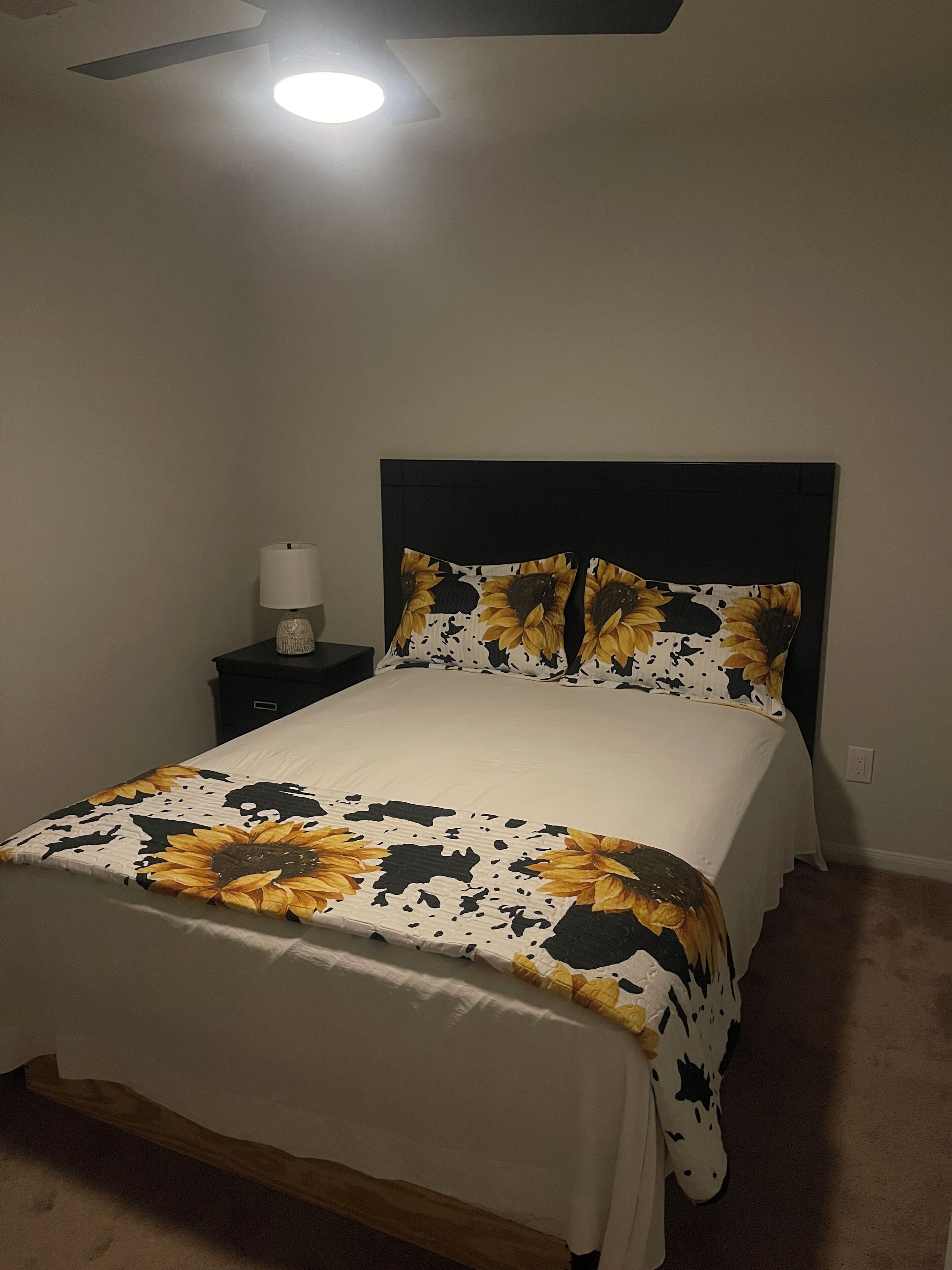 Ein Schlafzimmer mit einem Bett, einem Nachttisch, einer Lampe und einem Deckenventilator.