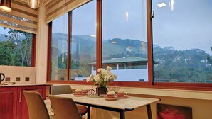 A modern kitchen with large windows, a dining table with chairs, and a vase of flowers. - Cozy 2-bedroom apartment in serene Kandy with AC (Kandy)
