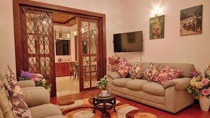 A living room with a sofa, a coffee table, and a TV. There is a door leading to a kitchen and dining area. - Cozy 2-bedroom apartment in serene Kandy with AC (Kandy)