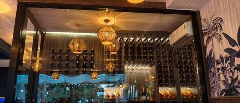 A restaurant with a wine rack, hanging lights, and a view of the city.