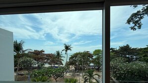 Une vue depuis une fenêtre donnant sur une plage bordée de palmiers, sous un ciel dégagé.