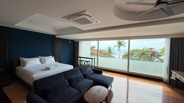 Une chambre d’hôtel moderne avec un grand lit, un canapé sombre, une petite table et une vue sur l’océan.
