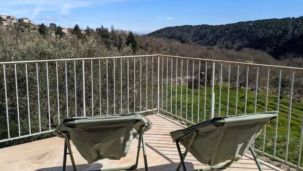 A balcony with two green chairs, a metal railing, and a view of a hilly landscape. - Typical stone house (Ribes)
