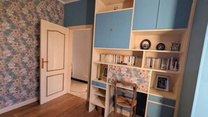 A room with a wooden floor, a desk with a chair, and a bookshelf. - Typical stone house (Ribes)