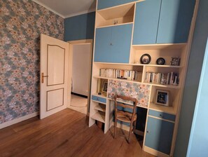 Ein Zimmer mit Holzboden, Schreibtisch mit Stuhl und Bücherregal.