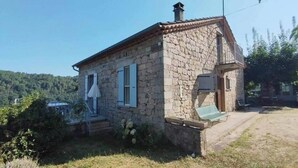 A stone house with a small porch, a chimney, and a door with a window. - Typical stone house (Ribes)