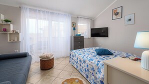 Ein Schlafzimmer mit Bett, Fernseher, Schreibtisch, Stuhl und einem Fenster mit Vorhängen.