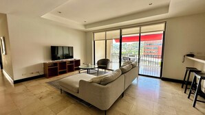 A living room with a sofa, TV, and a balcony with a red awning. - Spacious 2-BR apartment in the best location! (San Rafael de Escazú)