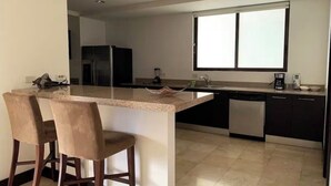 A modern kitchen with a central island, bar stools, a refrigerator, a dishwasher, and a window providing natural light. - Spacious 2-BR apartment in the best location! (San Rafael de Escazú)
