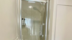 Une cabine de douche fermée par des parois en verre, avec une porte blanche, un sèche-mains et un flacon de shampoing fixé au mur.
