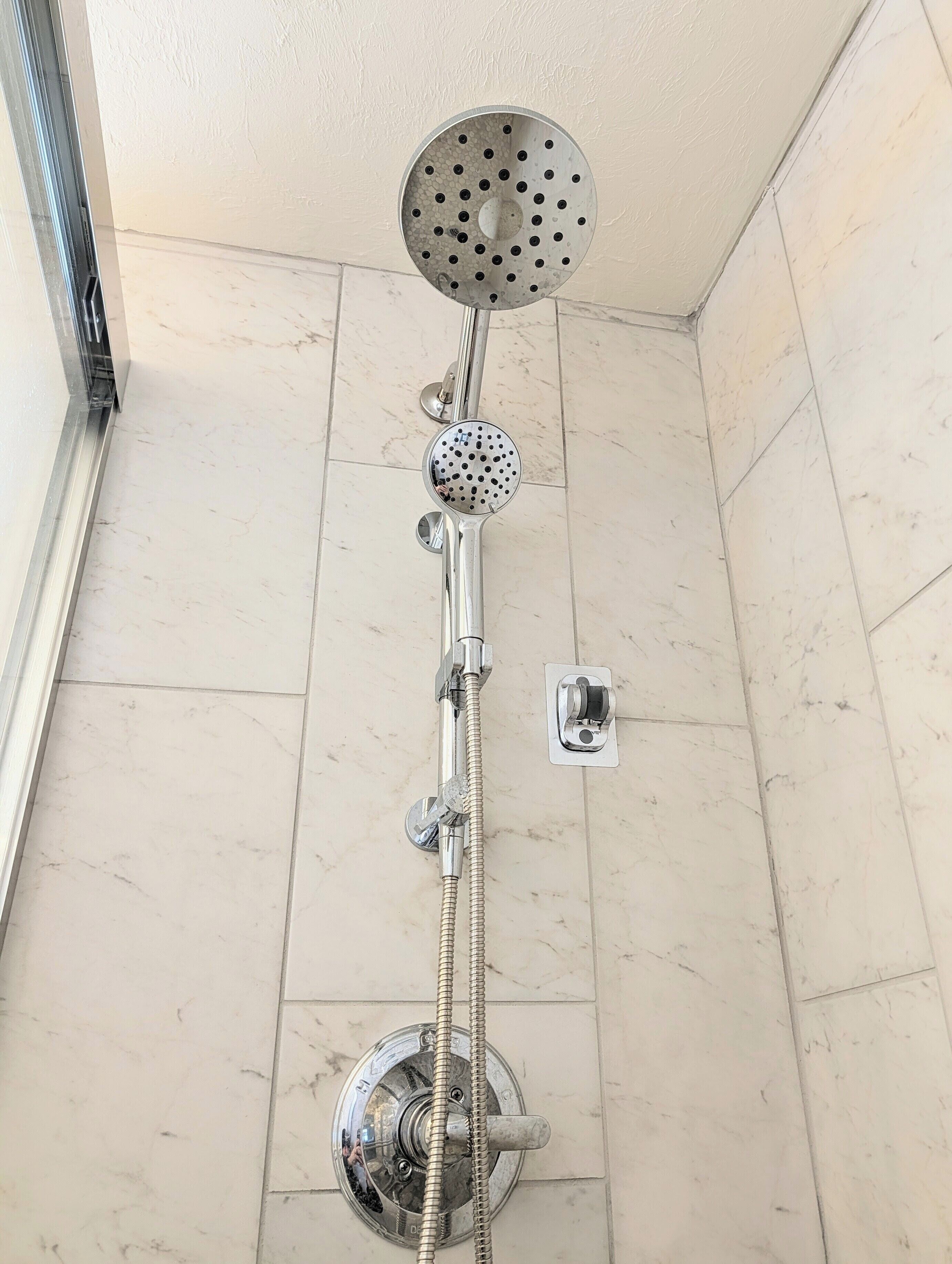 A shower with a handheld showerhead, a wall-mounted control panel, and a floor-mounted faucet.