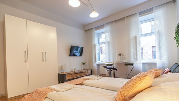 A bedroom with two beds, a TV, a desk, and a window with blinds. - Cozy 2BR City Retreat Central Location (Vienna)