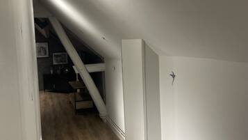 A narrow hallway with wooden flooring and white walls, leading to a staircase and a room with a large white cabinet.