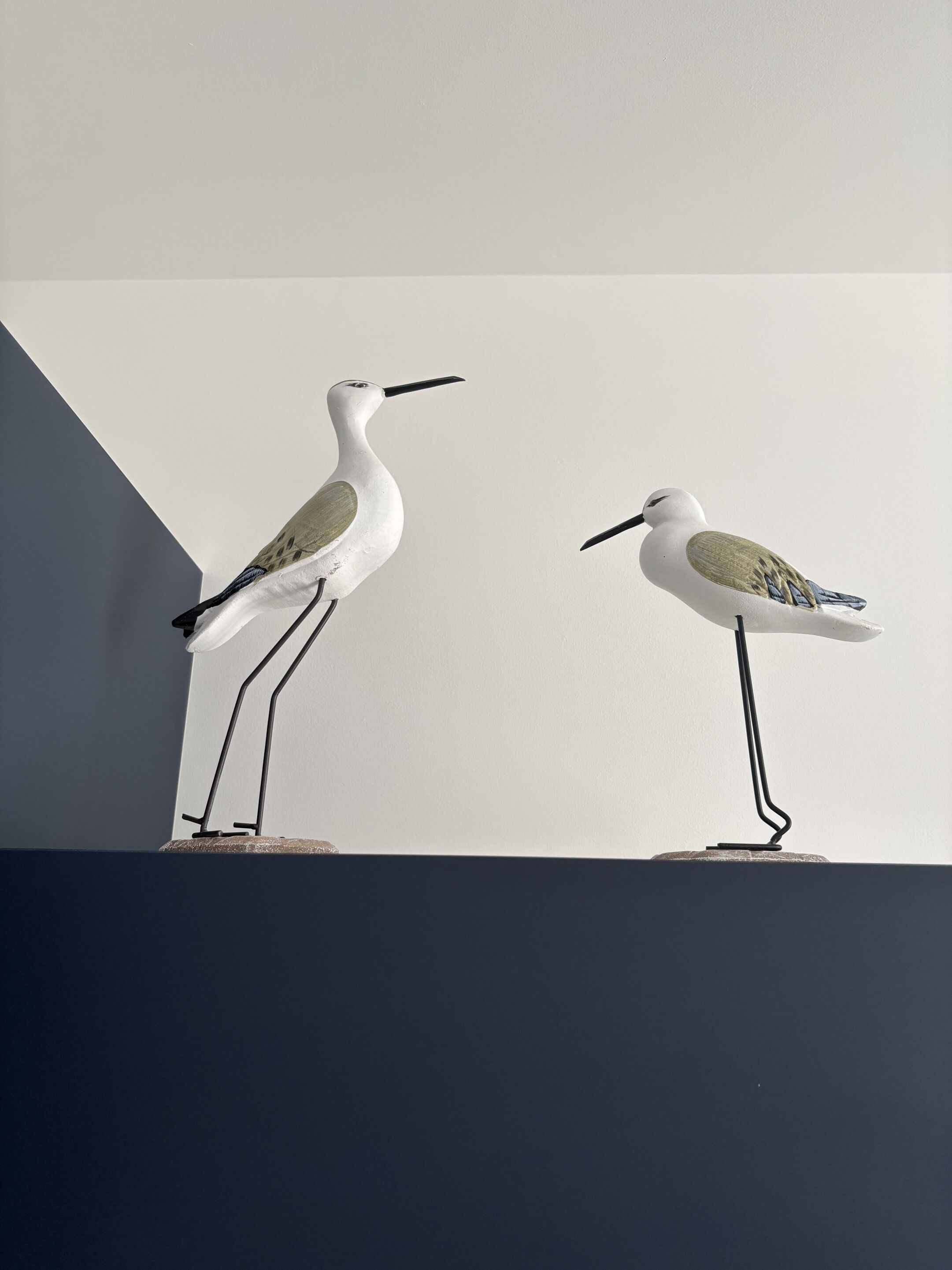 Two bird sculptures on a pedestal against a plain wall.