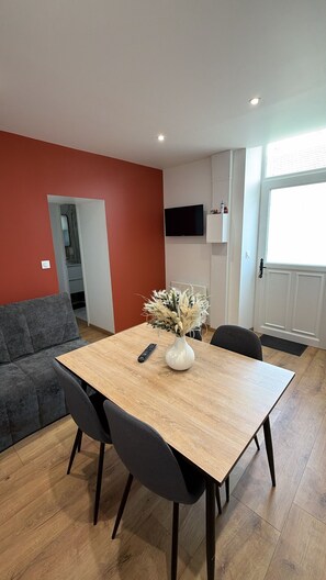 A modern living room with a wooden dining table, grey sofa, and a vase with dried flowers.