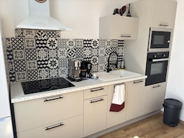 A kitchen with a patterned backsplash, a coffee maker, a sink, cabinets, a microwave, and an oven.