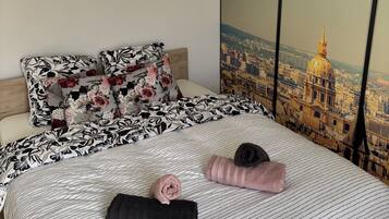 A neatly made bed with floral and striped bedding, a cityscape view through a window, and a wooden headboard.