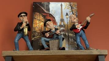 Three figurines of musicians on a shelf against a wall with a painting of Parisian street.
