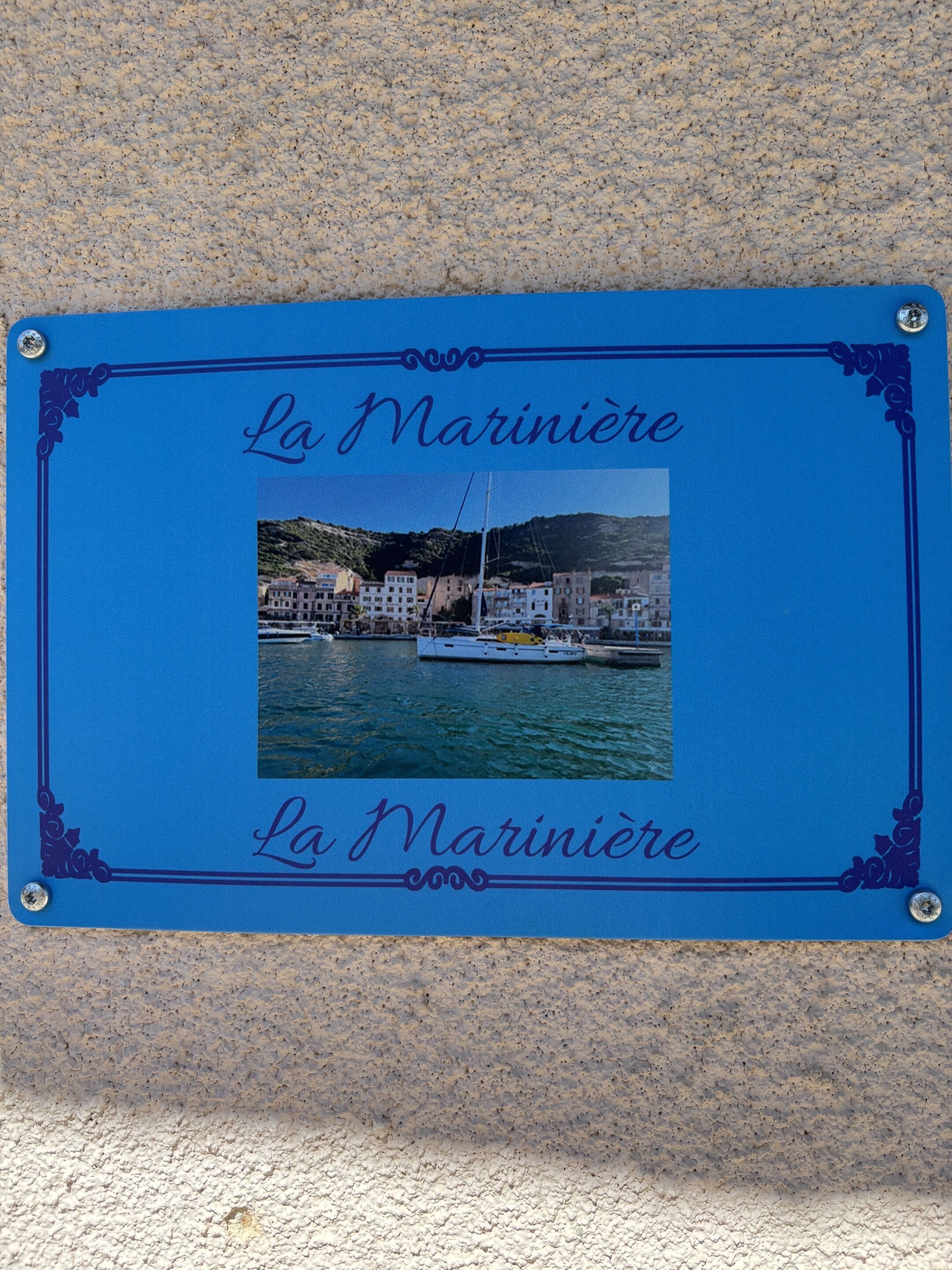 Un cartel enmarcado con el texto 'La Mariniera' y una foto de un pueblo costero con edificios y barcos.