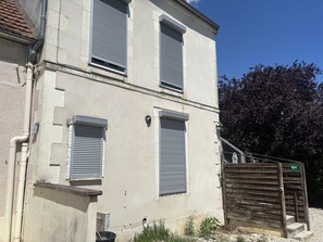 Un edificio con dos ventanas, un portón de madera y un árbol al fondo.