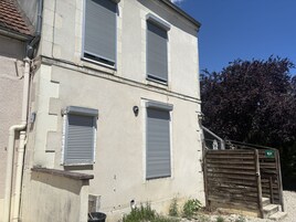 Un edificio con dos ventanas, un portón de madera y un árbol al fondo.
