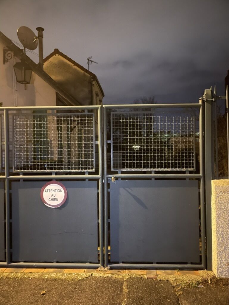 A metal gate with a sign that reads "ATTENTION AU CHIEN" (Attention Dog).