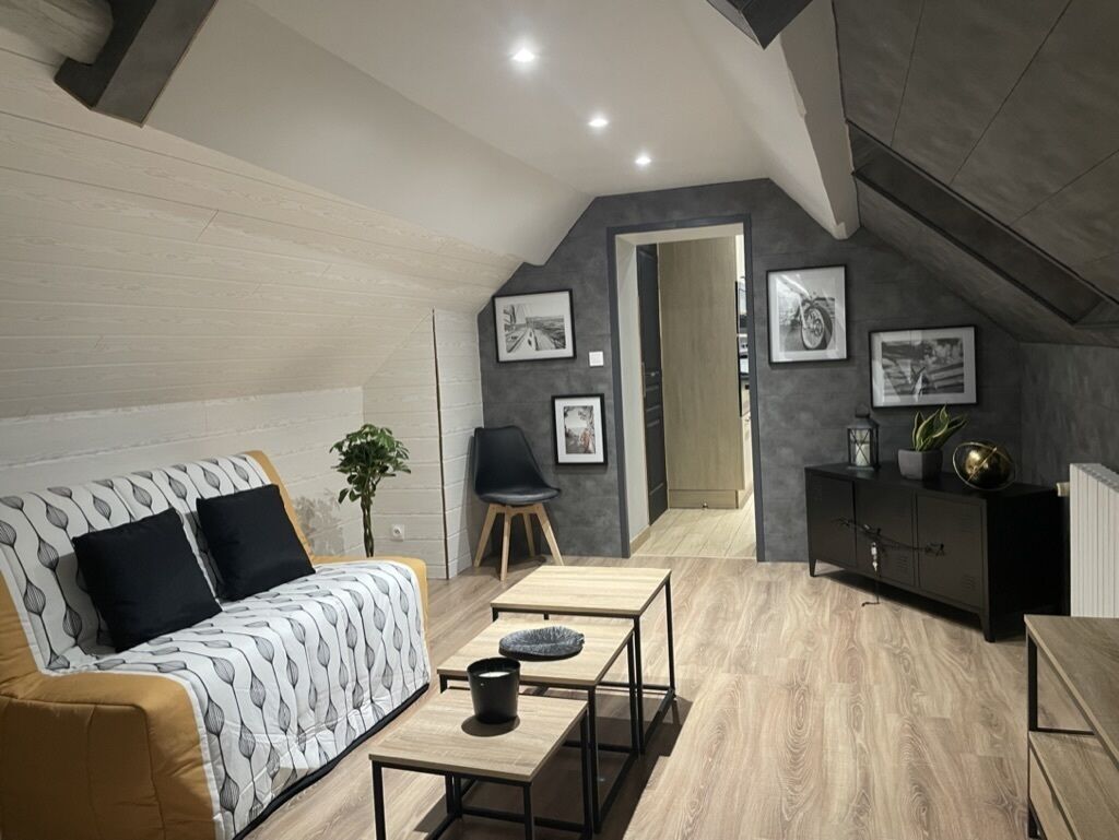 A modern loft bedroom with a sloped ceiling, a sofa, a dining table, and a black cabinet.