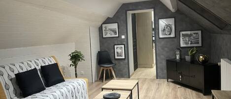 A modern loft bedroom with a sloped ceiling, a sofa, a dining table, and a black cabinet.