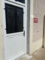Una puerta blanca con una reja metálica decorativa negra, una pared texturizada y un letrero de salida de emergencia rojo.