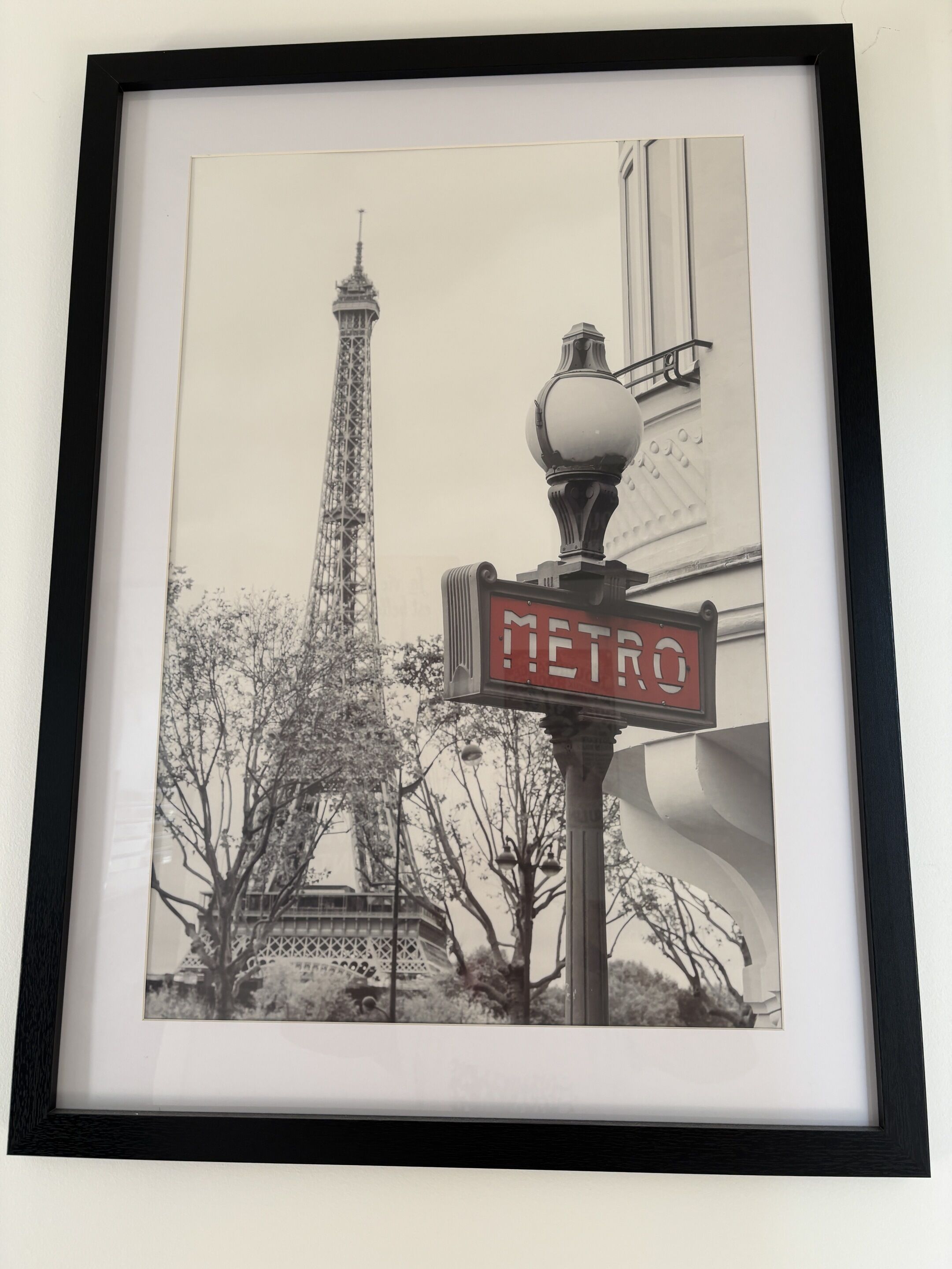 Une photographie encadrée de la Tour Eiffel, avec un panneau de signalisation indiquant « MÉTRO » au premier plan.