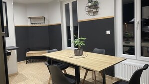 En matplats med ett träbord, svarta stolar, en krukväxt och en vägghylla med växter.