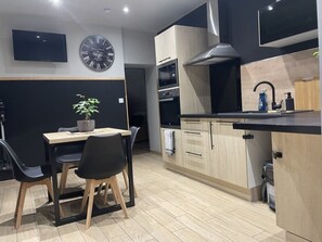 A modern kitchen with a dining area, featuring a clock, a TV, and a plant. - L'Escale Féerique (Auxerre)