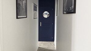 En smal hall med vita väggar och en mörkblå dörr längst ner. Det hänger tre inramade tavlor på väggarna.