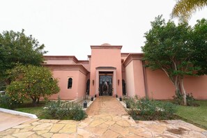 Um edifício com entrada central, ladeado por árvores e um caminho de pedra que leva à porta.