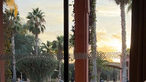 A room with a bed, a view of a pool, palm trees, and a gazebo.