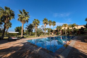Piscina com palmeiras e um edifício ao fundo.