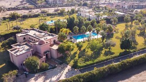 An aerial view of a resort with multiple buildings, a swimming pool, and well-maintained gardens.